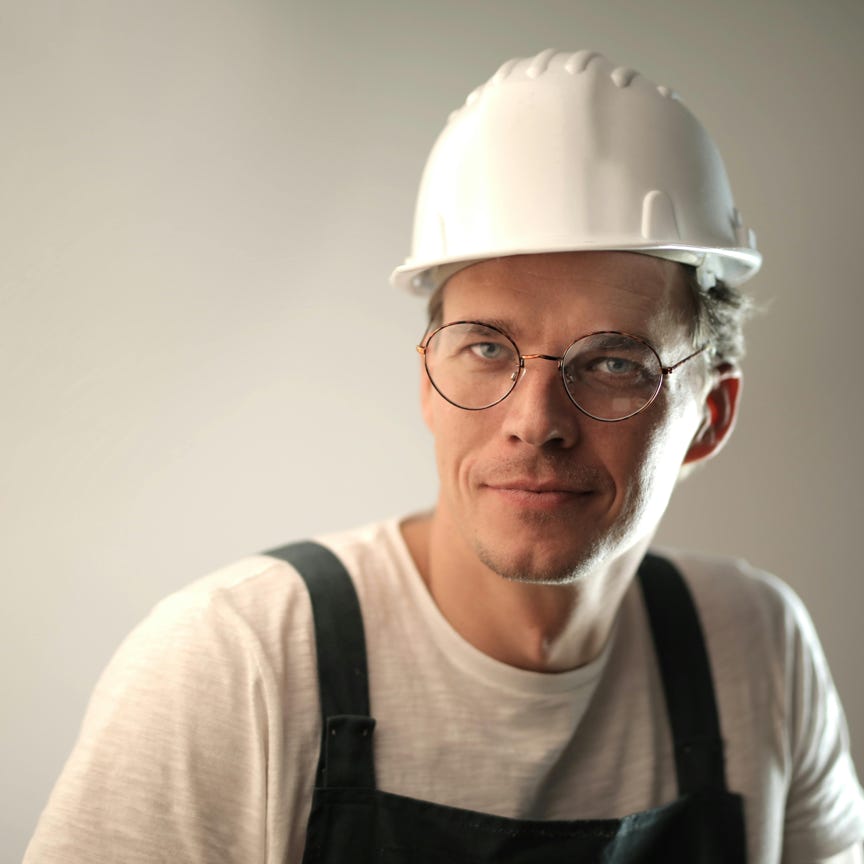 Content male builder in workwear and hardhat smiling on gray background in studio and looking at camera